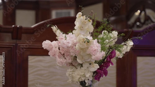 A close-up of an elegant bouquet with pink, white, and purple flowers against a warm wooden background. This romantic scene is perfect for weddings, events, or interior design concepts.
