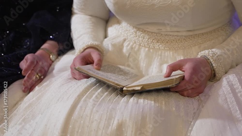 A close-up of a bride in a white lace dress holding a prayer book. This intimate and serene moment captures tradition and faith, ideal for wedding or religious-themed content.