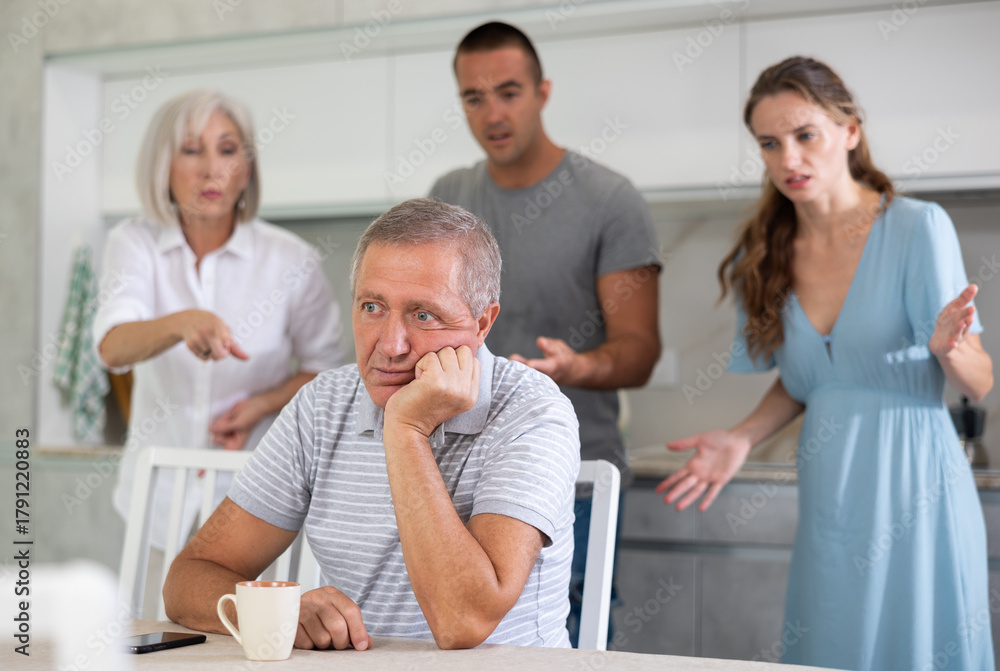 Fototapeta premium Adult man sits at table in kitchen and pretends that he does not hear anything from his relatives