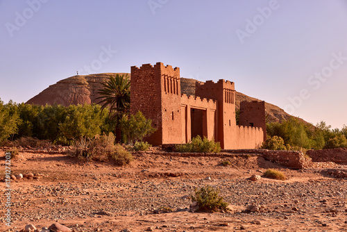 Ait ben haddou kasbah stands in the desert landscape with its traditional clay architecture. The dry riverbed is visible in front, under a clear sky in Morocco