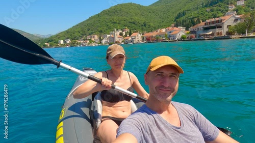 Couple kayaking in the bay of kotor, montenegro, taking selfies. Tourists paddling an inflatable kayak in the bay of kotor, enjoying summer holidays in montenegro, taking selfies