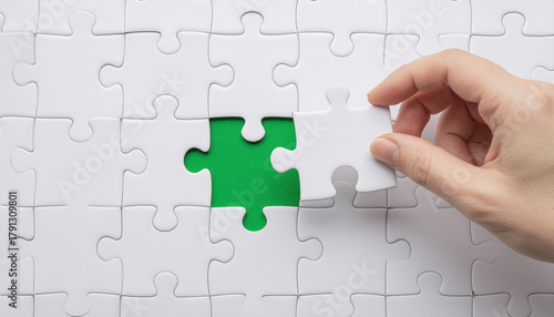 Hand placing the last white puzzle piece into a green gap, symbolizing problem-solving, completion, teamwork, and strategy. Perfect for business, planning.