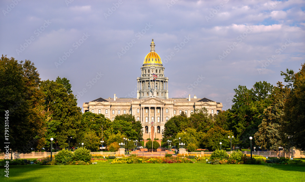 Obraz premium Colorado State Capitol building in Denver, Colorado. The gold dome is lit by evening sun, with a green lawn and park in the foreground under a cloudy sky