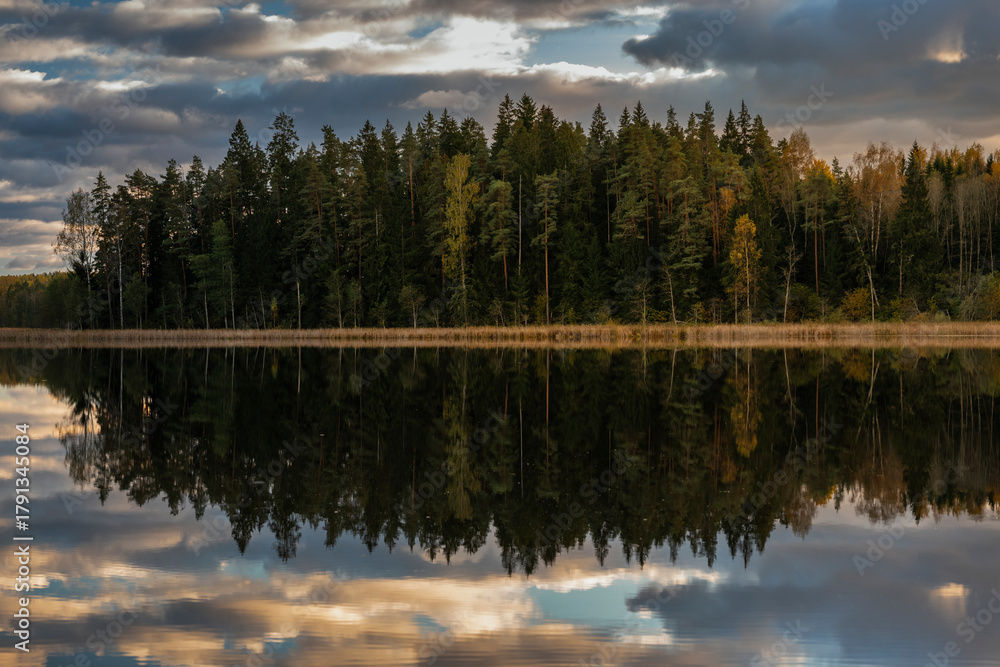 Fototapeta premium Colourful autumn landscape in the forest next to a lake during sunset, water reflections and colourful sky