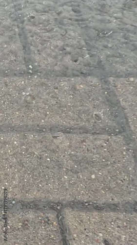 Wallpaper Mural Raindrops continuously hit stone pavement forming circular ripples and glistening wet surface texture representing rainy weather and natural motion of water Torontodigital.ca