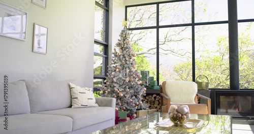 Camera is starting to pan right in living room, revealing Christmas tree, wrapped gifts, fireplace