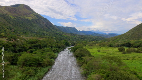 Fotografie Aerial drone view of the Río Bogotá (Bogotá River) flowing through a vibrant green valley surrounded by steep, lush mountains near Apulo, Cundinamarca, Colombia
