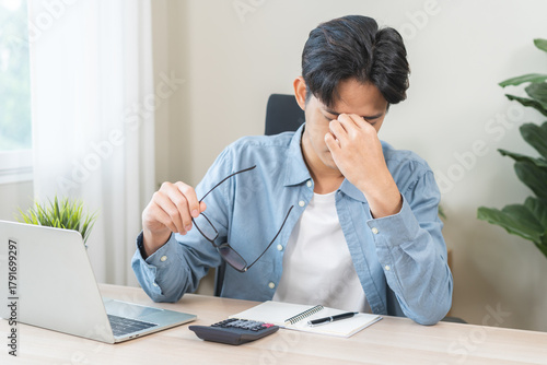 Eye problem concept, fatigue asian young man, male tired eyes, irritated rubbing nose, relief vision pain after work on laptop computer, eye strain, hand holding glasses, suffer migraine, bad blurry.