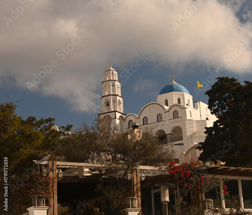 The national flag of Greece flying in front of a blue church steeple.