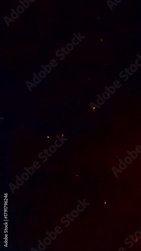 Small red embers rise and move in dark smoky night atmosphere creating floating glowing particles from distant fire with dynamic warm light and cinematic texture