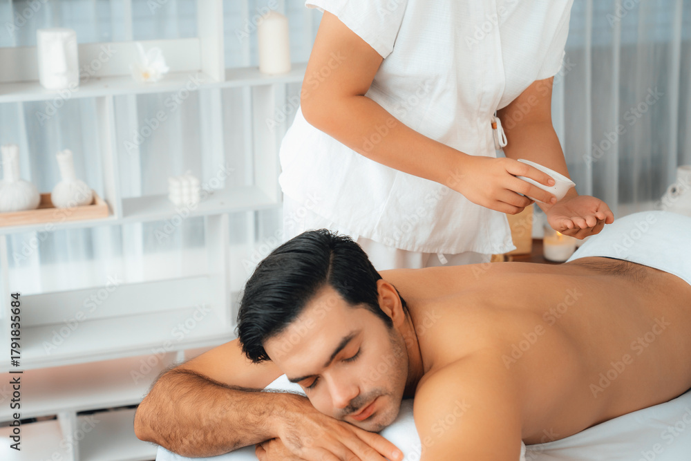 Fototapeta premium Caucasian man customer enjoying relaxing anti-stress spa massage and pampering with beauty skin recreation leisure in day light ambient salon spa at luxury resort or hotel. Quiescent