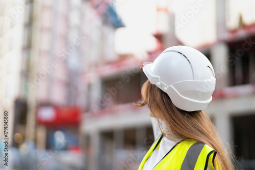 Woman builder in white helmet observes building progress at construction site