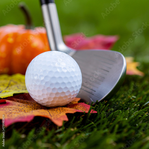 Golf ball and club on autumn leaves with pumpkin in the background