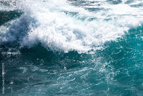 Fototapeta Naklejka Na Ścianę i Meble -  Close up of ocean wave with white foam. Sea splash and turquoise water. Ocean waves in motion. Blue wave rolling with reflections. Texture of seawater and foam. Powerful sea wave background.