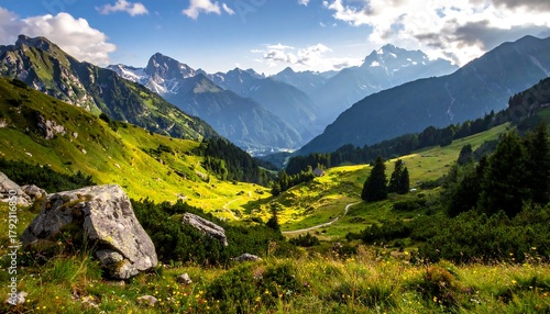 Fototapeta Naklejka Na Ścianę i Meble -  A scenic vista of mountains, valleys, and green meadows under a sunny sky. A winding road cuts through the landscape