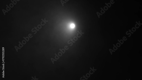 Dynamic spotlight beam of light moving across a dark, smoky background, creating an abstract, volumetric light effect in a black and white monochromatic animation