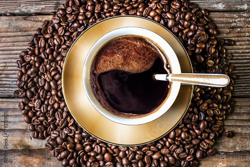Aromatic coffee cup surrounded by freshly roasted coffee beans on wood