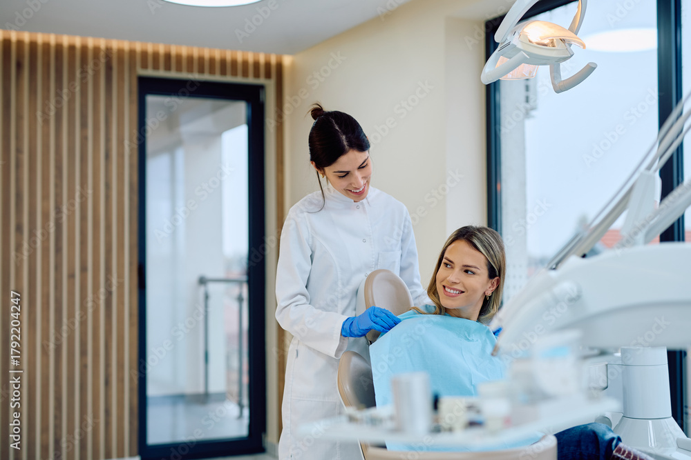 Obraz premium Female dentist helping patient sitting in dental chair for examination, promoting dental healthcare and oral hygiene