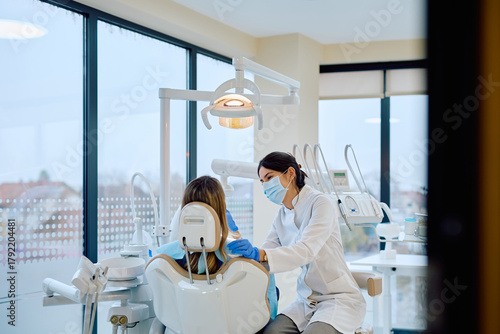 Dentistry professional in a mask and gloves preparing to examine a female patient in a modern dental office