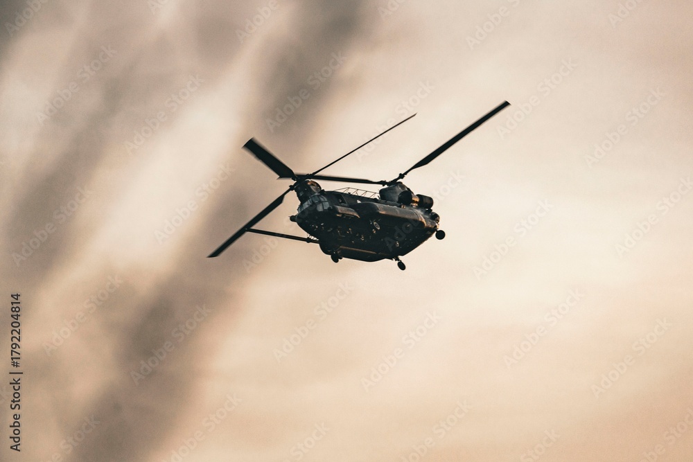 Fototapeta premium Military helicopter flying over a cloudy sky with a vintage sepia tone effect creating a dramatic atmosphere