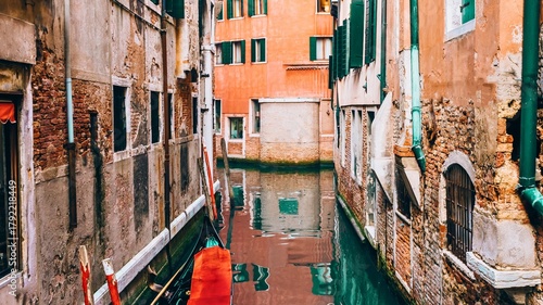 Narrow venetian canal lined with old buildings and reflections