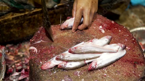 Close-up of worker slicing and preparing fresh fish with large knife on wet market chopping block.
