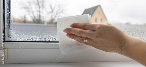 Woman's hand wiping condensation and water drops from a foggy window with a paper towel