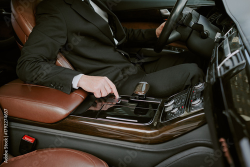 Obraz na plátne Caucasian middle aged man sitting in luxury car, wearing business suit, operatin