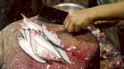 Close-up of worker slicing and preparing fresh fish with large knife on wet market chopping block.