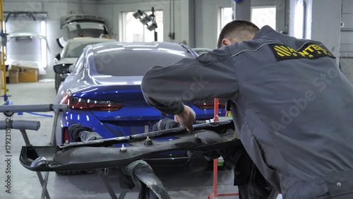 A mechanic attaches a plastic bumper guard in a workshop in front of a car brought in for body repair 
