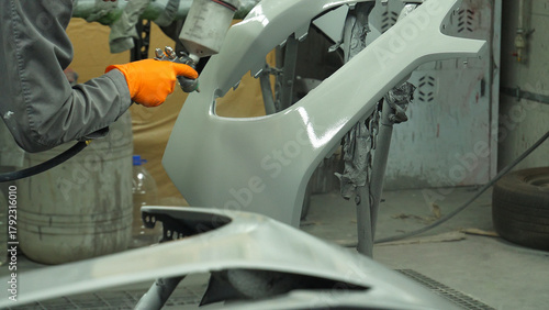 Paint technician spray paints a car front bumper using a paint gun with a diffuser  
