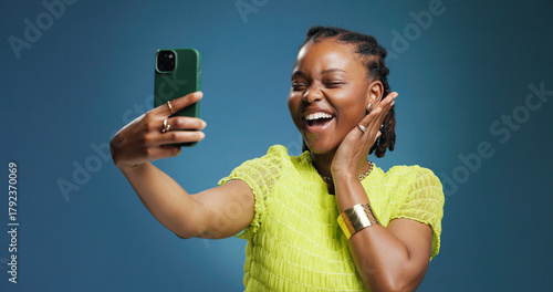 Selfie, smile and social media with black woman in studio for profile picture or status update. App, excited and photograph with African content creator on blue background for streaming platform