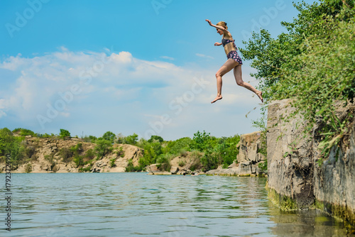 Active woman jumping into water from a cliff enjoying summer vacation. Woman in swimsuit jumps off cliff into lake, freedom and excitement