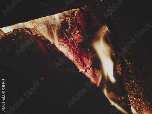 Direct view into fireplace with focus on glowing embers, blurred charred log on right for text space, soft flame on left, warm matte tones, cozy rustic atmosphere, intimate fire detail.