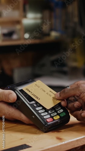 Vertical closeup of hand of unrecognizable customer paying for purchase with credit card, tapping it on terminal cashier holding