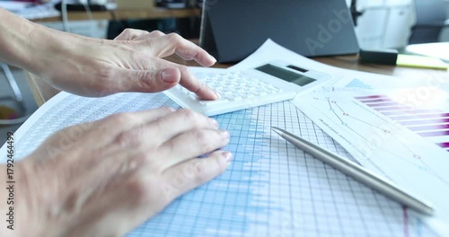 Accountant hand presses calculator buttons on finance charts near spreadsheet. Worker verifies totals and enters figures preparing monthly report