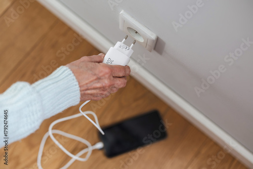 Close-up of senior woman inserting a power plug into a socket to charge her phone

