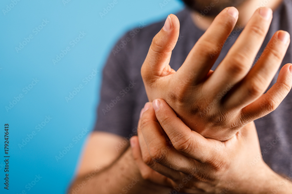 Fototapeta premium Close-up of a man holding his painful wrist, shows discomfort and medical concern, potential for injury and treatment, background blue.