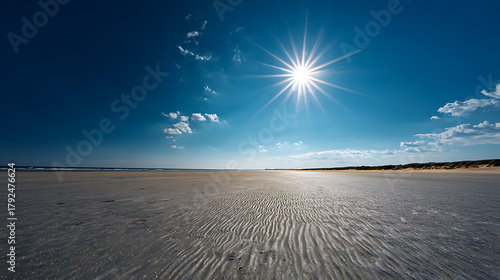 Fototapeta Naklejka Na Ścianę i Meble -  Vast sandy beach under bright sun and blue sky with scattered clouds ocean water