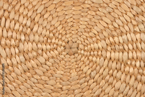 A full-frame, detailed close-up of a natural light brown woven texture with a central circular pattern of tightly braided plant fibers
