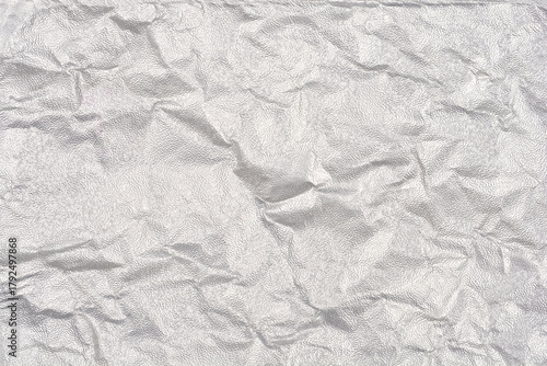 A full-frame, close-up abstract background of heavily crumpled and textured silver metallic foil with numerous folds and wrinkles
