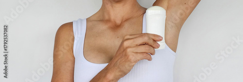 Bild auf Leinwand Woman applying deodorant while wearing a white crop top