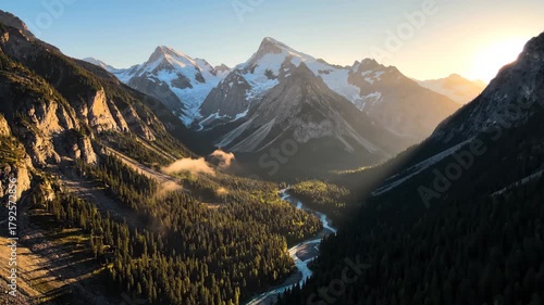 Glacial river carves a winding path through a broad alpine valley of dense spruce forests and towering snow-capped peaks, bathed in golden sunrise light and crisp blue sky