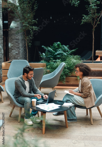 startup pitch rehearsal in cozy lounge, practicing investor presentation with printed deck and laptop, mentor