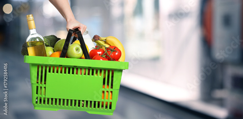 Bild auf Leinwand Customer holding shopping basket with different food products at supermarket, closeup