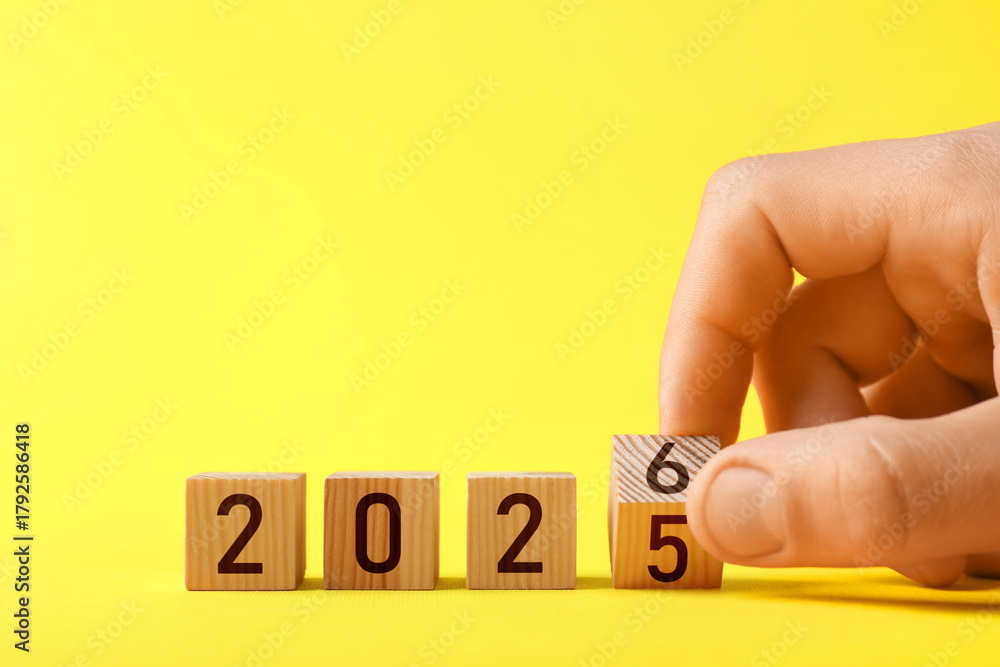 Obraz premium New Year. Man flipping cube with numbers 5 and 6 to make 2026 on yellow background, closeup