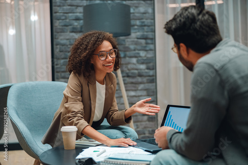 smiling consultant advising client in modern office, relaxed coaching session with laptop, documents, coffee