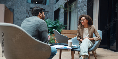 two professionals meeting in atrium over coffee and documents, exchanging roadmap ideas and strategic feedback