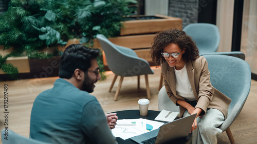 two colleagues analyzing documents at table, cross-referencing charts and metrics while developing strategy