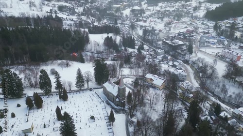 Experience a stunning aerial perspective of the Church of St. Peter and Paul in Tanvald during winter. The snow-covered landscape creates a serene atmosphere around this historic site.